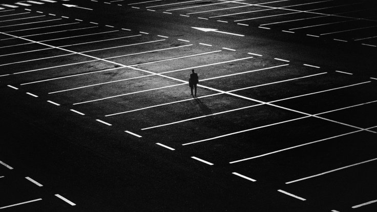 Black and White Photograph. Person standing alone in a parking lot, low lighting.