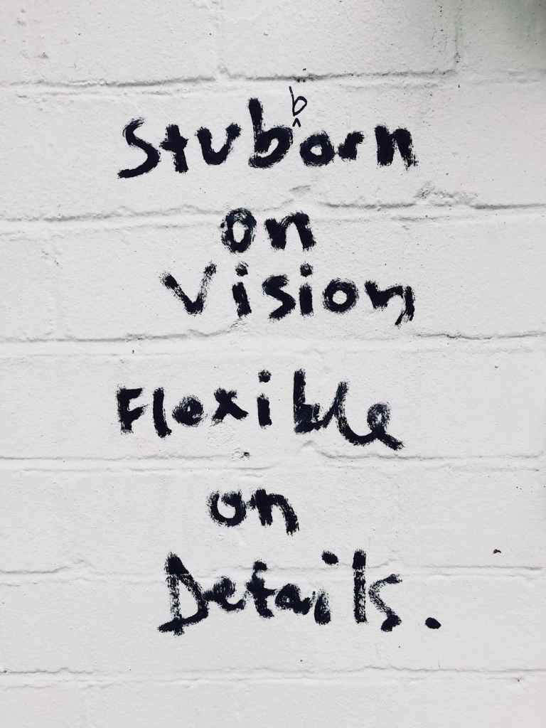 A white wall with the words 'Stubborn on vision flexible on deadlines' written on